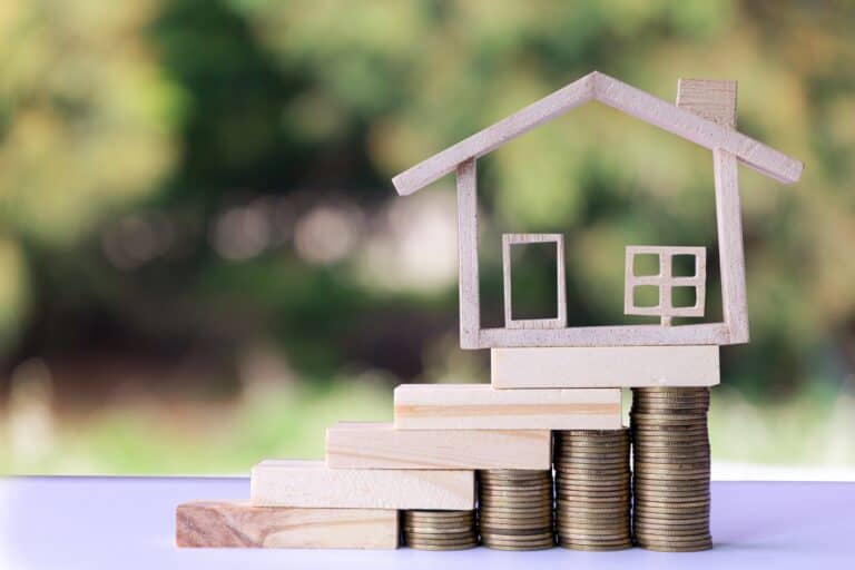 A wooden house figurine with wooden stairs and stack of coins in the concept of affordable housing options in Greenwich.