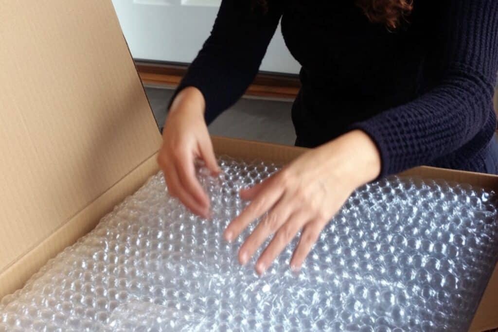A woman placing bubble wrapped items into a box in the concept of 'How to Pack and Unpack for a Home Removal Efficiently When Moving to Greenwich'.