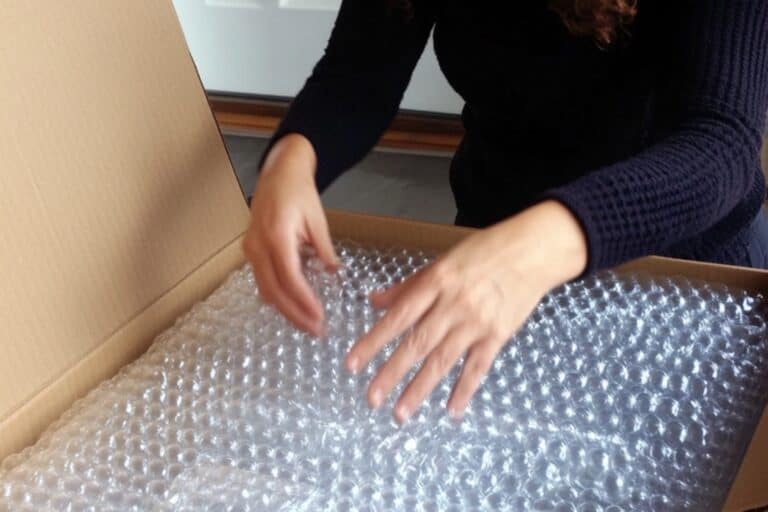 A woman placing bubble wrapped items into a box in the concept of 'How to Pack and Unpack for a Home Removal Efficiently When Moving to Greenwich'.
