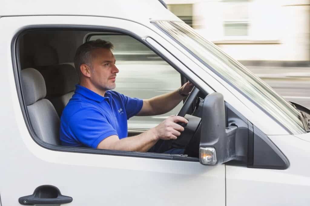 A man wearing a blue polo shirt driving a white van in London
